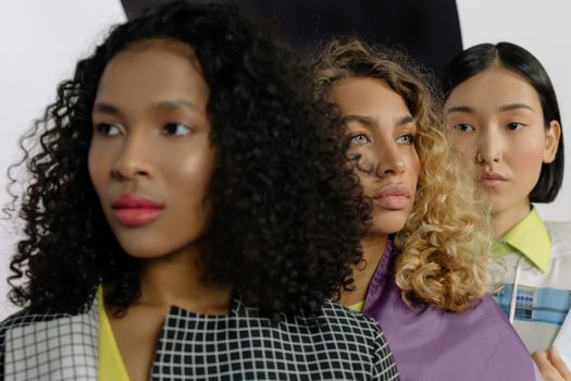 Three stylish women posing together in a studio setting emphasizing diversity and modern fashion.