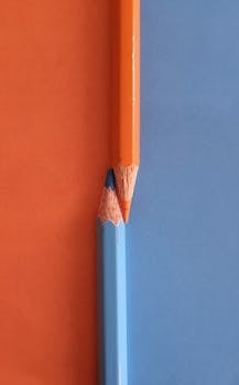 Minimalist composition of orange and blue pencils on matching blue and orange surface.