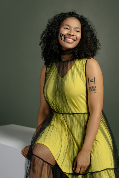 Free Portrait of a smiling woman in a yellow dress advocating for human rights in a studio setting. Stock Photo