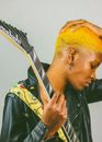 Side view of crop stylish African American female musician with short dyed hair in leather jacket touching head while standing against white background with electric guitar
