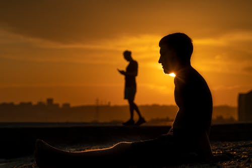 Free Silhouette of Man Sitting on Sand during Sunset Stock Photo