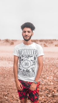 Casual portrait of a stylish young man in a desert landscape in El Jadida, Morocco.