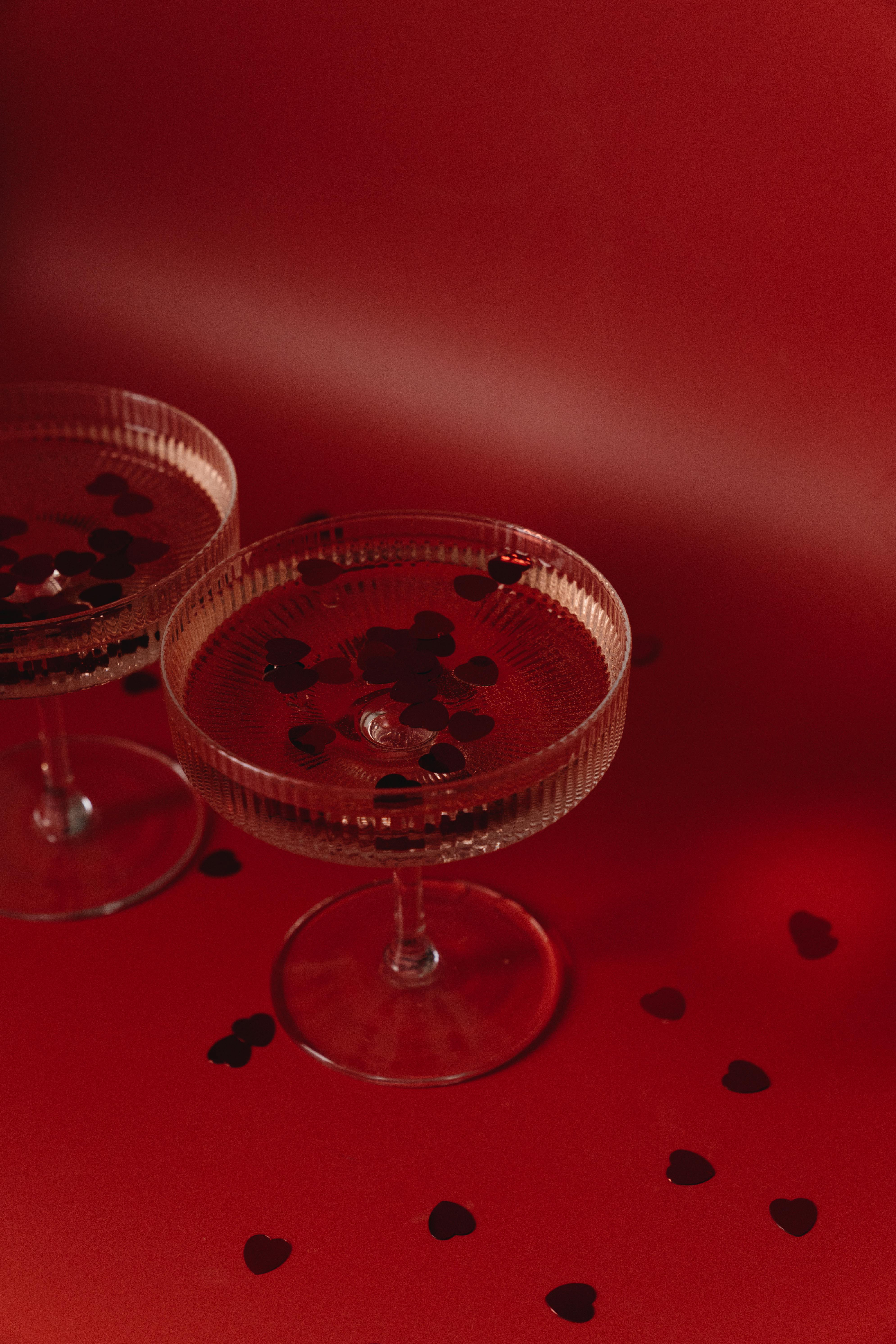 Two elegant wine glasses with heart-shaped confetti on a vibrant red background.