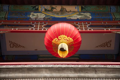 Free Red Chinese lantern hanging under a decorated building entrance, signifying cultural heritage. Stock Photo