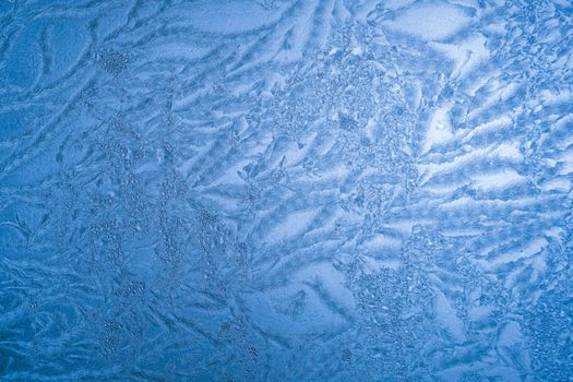 Intricate frost formations on a glass window, captured in cold winter light.