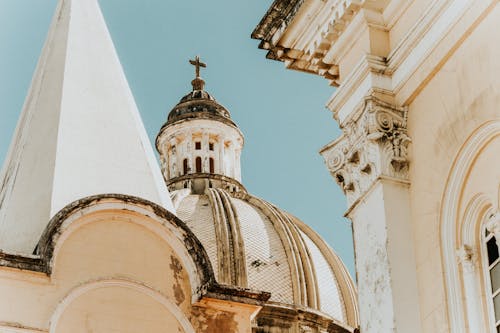 Low angle of aged Christian church with cross and dome with ornamental details and white stone walls in sunny day under blue cloudless sky