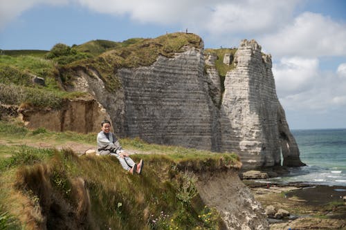 Smiling Asian woman sitting on rocky coast near sea