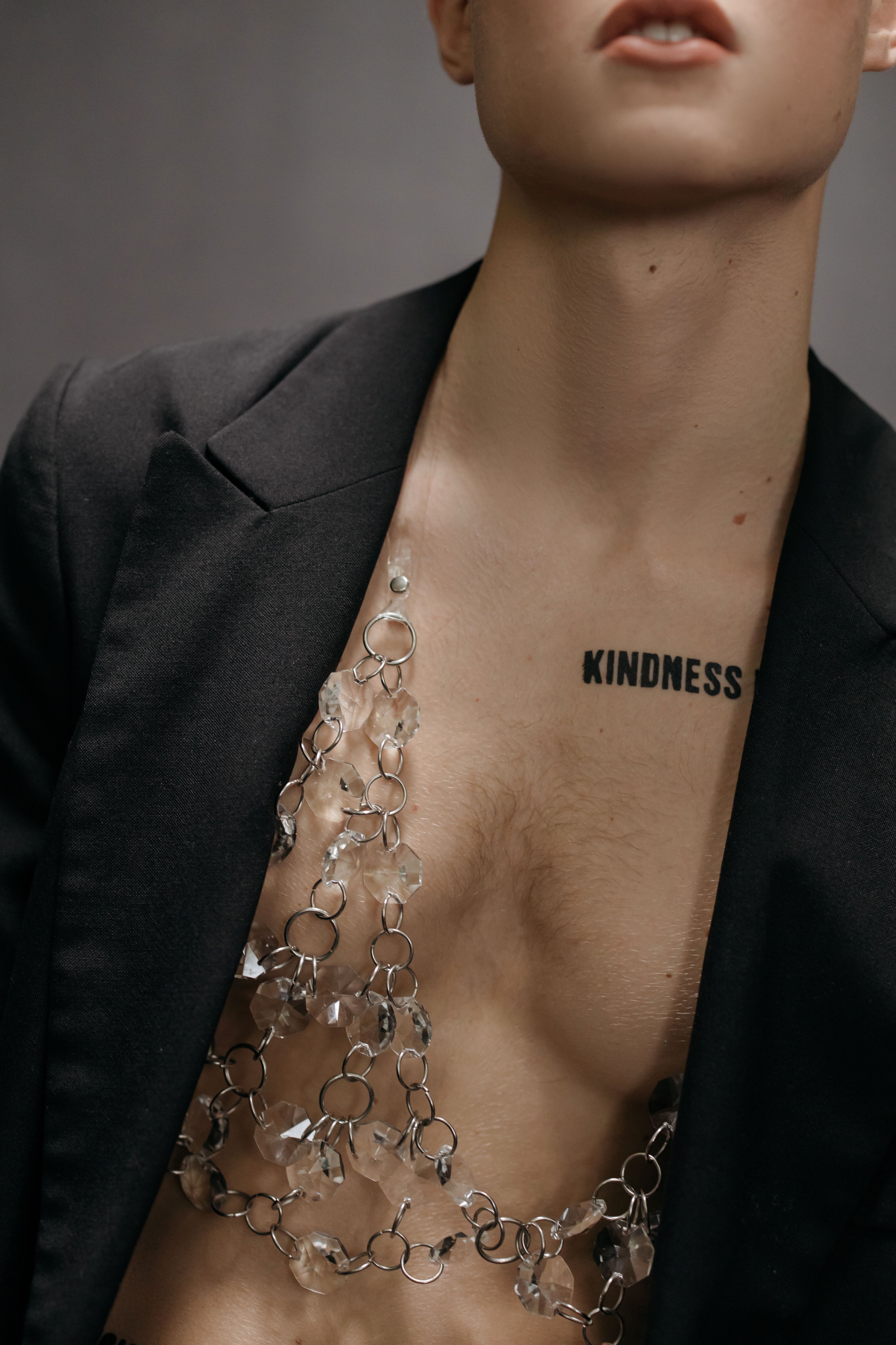 Fashionable male model with 'Kindness' tattoo and jewelry, showcasing confidence and elegance.