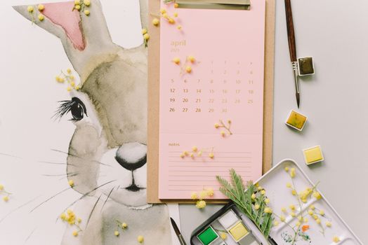 A watercolor Easter bunny illustration beside an April calendar and mimosa flowers, perfect for spring celebrations.