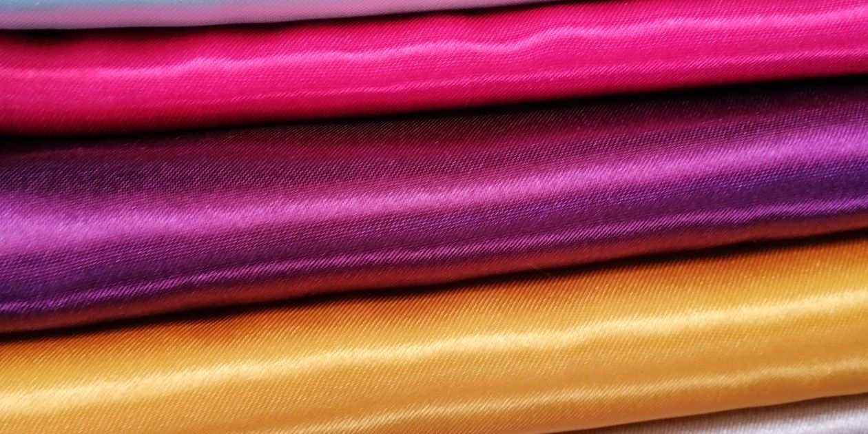 Nhiều lớp vải satin màu bạc, hồng, tím, vàng và tím nhạt xếp chồng lên nhau, mỗi lớp phản chiếu ánh sáng theo cách riêng
