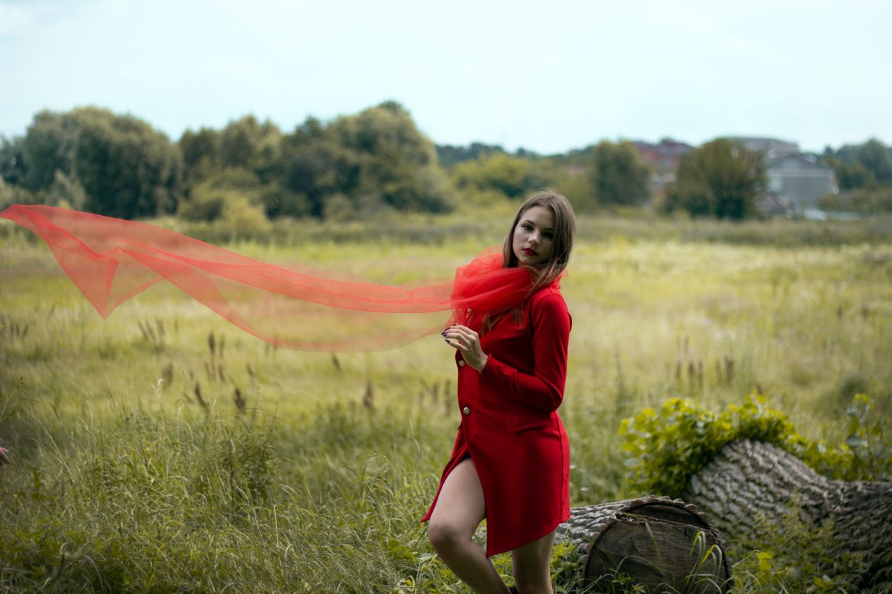 elegant woman in red coat and scarf posing outdoors in a green field