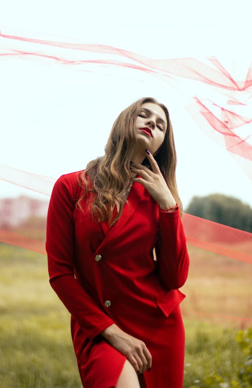 Photo of a Woman in a Red Coat Posing with Her Eyes Closed