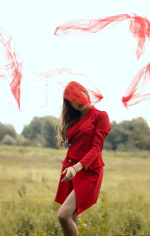 Photo of a Woman in a Red Coat Posing Under a Red Sheer Fabric