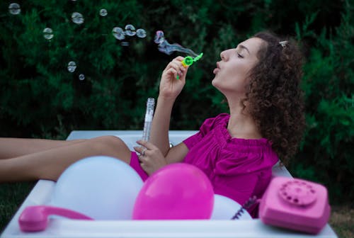 A Woman in Purple Top Blowing Bubbles from a Toy