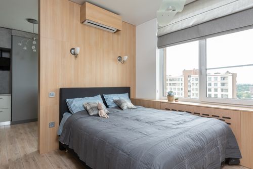 Free Interior of light contemporary apartment with bed with pillows and soft bunny toy near window with windowsill with decorative objects with jalousie near air conditioner and entrance to kitchen Stock Photo