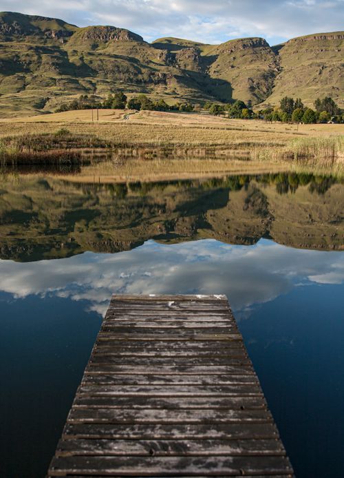Free Peaceful lake reflecting mountains and sky, featuring a wooden dock. Stock Photo