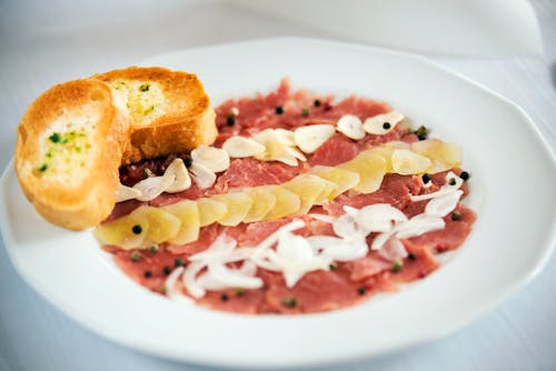 Tasty appetizer of carpaccio with raw onion and ginger slices with black peppercorns on plate in restaurant on white background