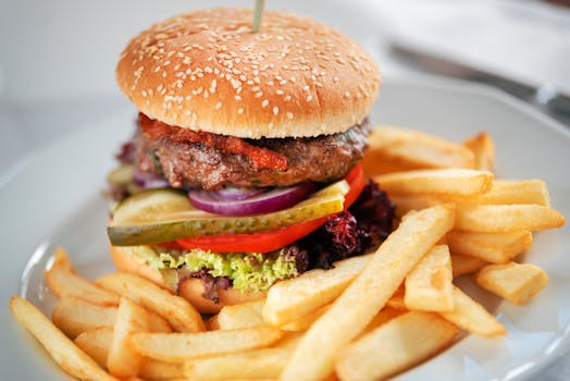 Tasty burger with juicy patty and tomato with pickle slices between buns with sesame seeds near deep fried potato sticks