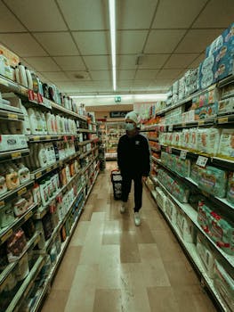 Man wearing mask shopping in a grocery store aisle with a basket.