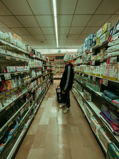 Free A man shop in a grocery store aisle, holding a basket with various products. Stock Photo