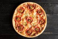 Overhead view of appetizing pizza with pepperoni and green chili pepper pieces on wooden surface