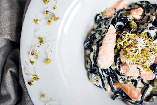 Fresh gourmet salmon and black pasta with cream sauce and sprouts served on a white plate.