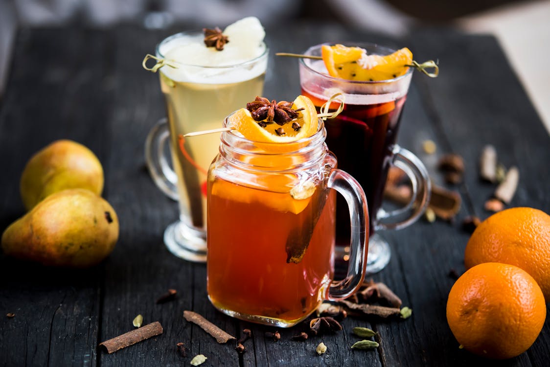 Free Jar and glasses of mulled wine drinks with fresh orange and pear slices on skewers on table with dry condiments Stock Photo