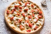 From above of yummy pizza with pickled capers and fresh tomato slices on table with spilled flour