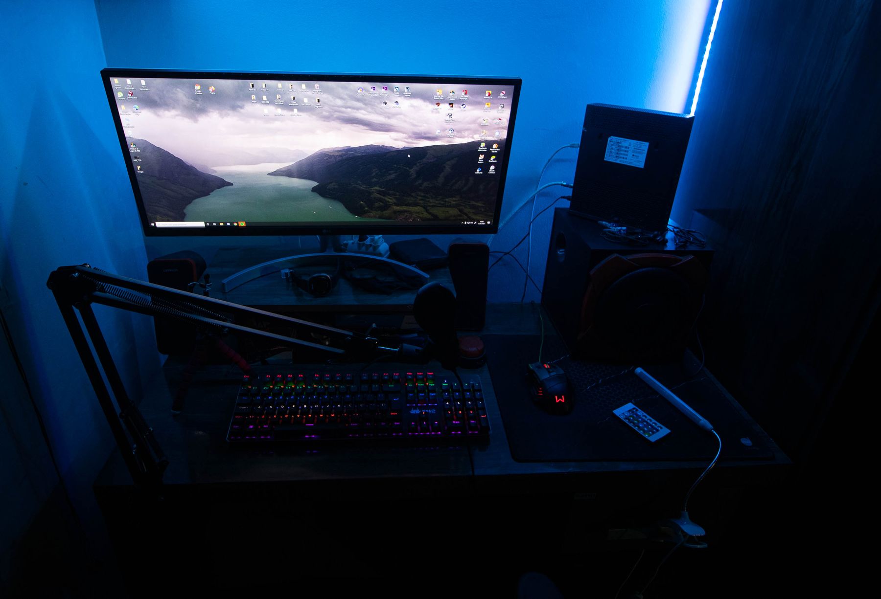 Organized gaming desk with ultrawide monitor, gaming keyboard, mouse, microphone arm and illuminated desktop hardware