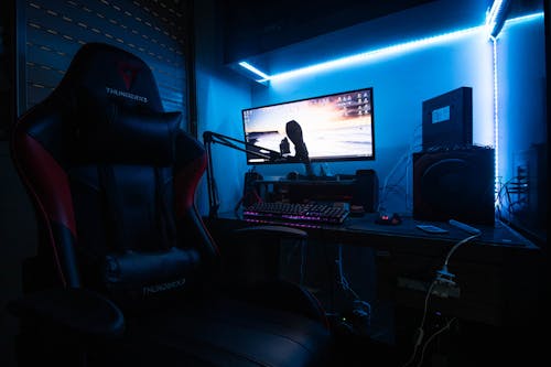 Free Desktop Computer with Speakers and Gaming Chair in a Room with Blue Light Stock Photo