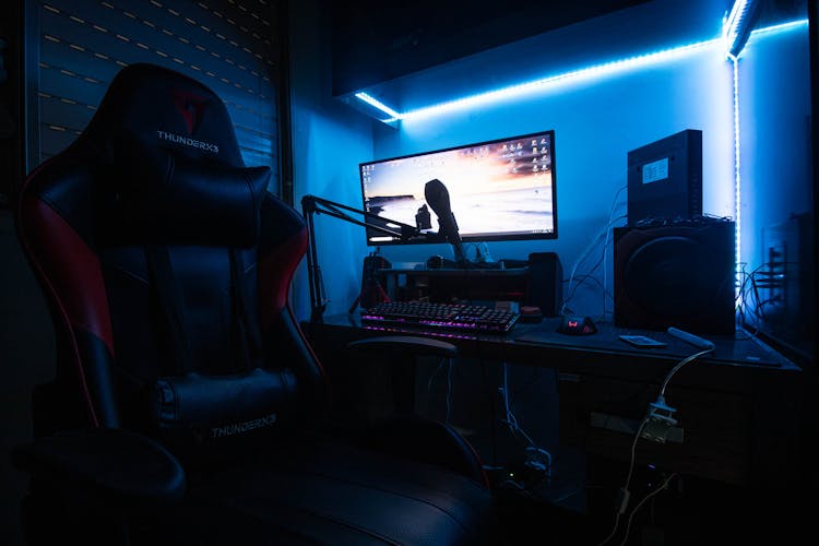 Desktop Computer With Speakers And Gaming Chair In A Room With Blue Light