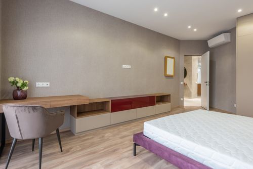 Free Soft bed with mattress placed against wooden table with decorative flowerpot in spacious stylish bedroom with opened door at home Stock Photo