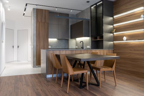 Table and chairs placed near modern kitchen counter with cupboards in stylish apartment with white doors in corridor at home