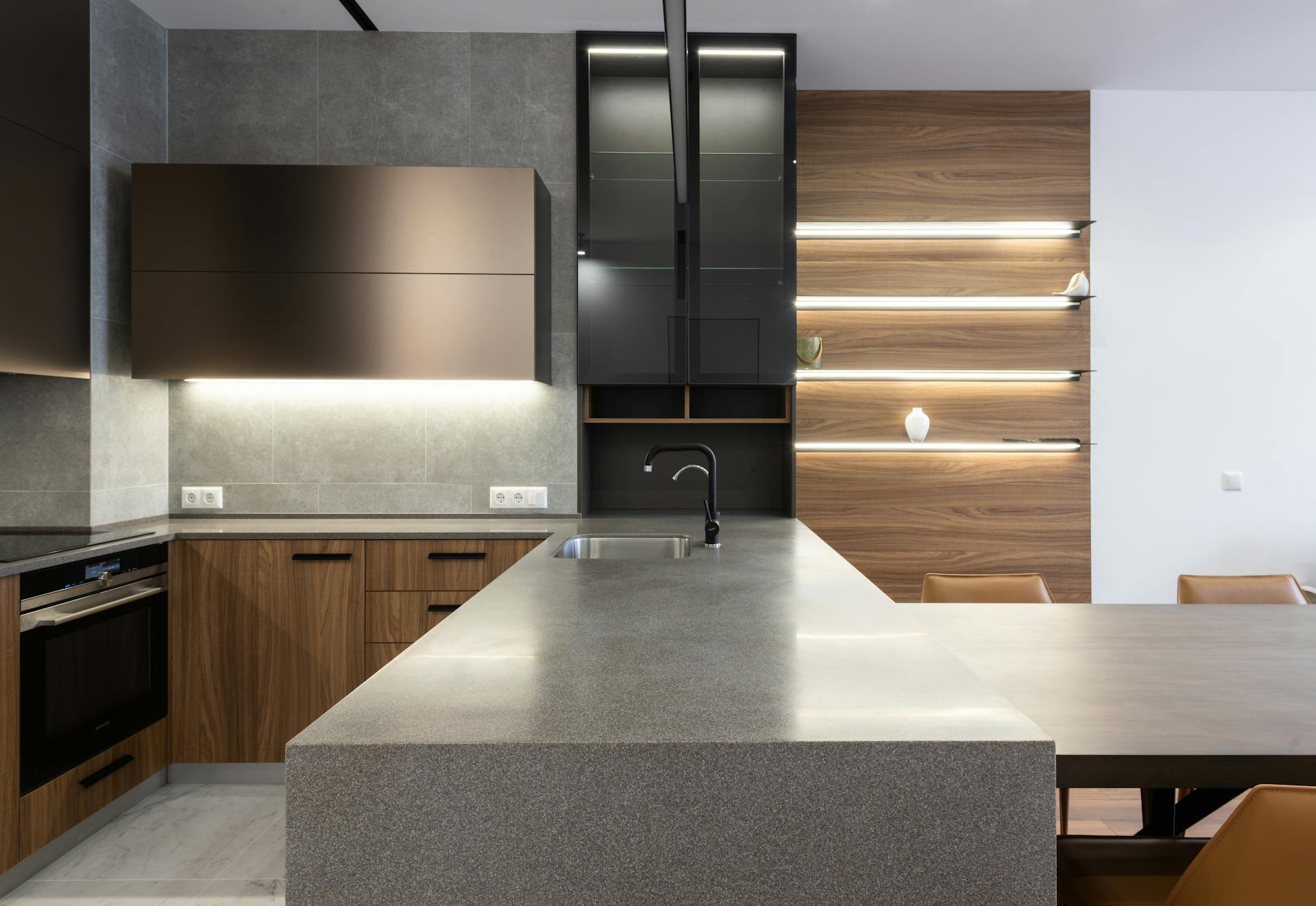 Wooden cupboards with stove placed near gray counter in modern kitchen with light decoration on wall and table in apartment