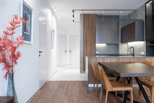 Interior of contemporary apartment with wooden table and chairs placed near modern kitchen with appliances in spacious flat with doors