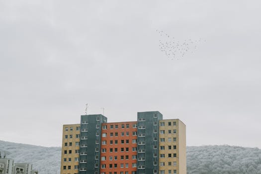 Colorful apartment building with birds flying in a cloudy sky.