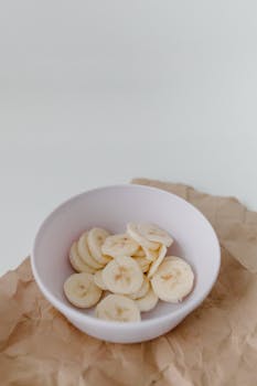 Aesthetic arrangement of banana slices in a bowl on brown paper, perfect for food themes.