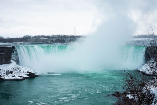 Snowy view of Niagara Falls with mist and icy surroundings captured in winter.