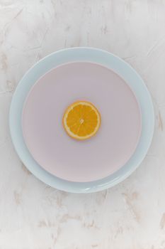 Top view of an orange slice on stacked ceramic plates, minimalist aesthetic.