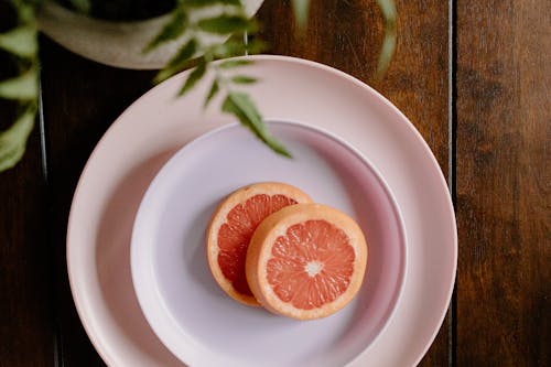 Top view of fresh juicy grapefruit slices placed on white ceramic plate served on wooden table near potted plant