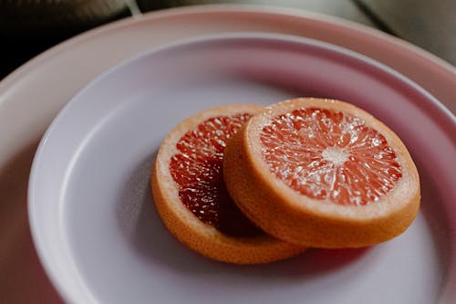High angle closeup of peaces of fresh healthy grapefruit arranged on ceramic plate in sunlight