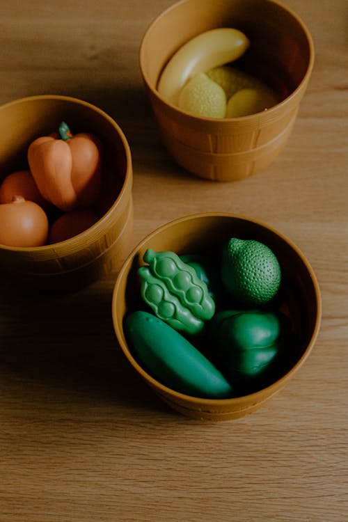 High angle of assorted multicolored toy veggies and fruits stacked in plastic pots placed on wooden table