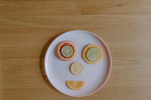 Top view of plastic plate on wooden table with colorful sliced grapefruit orange lemon and lime creating happy face