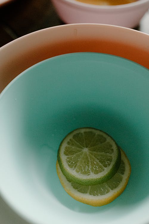 From above slices of fresh healthy lemon and lime placed in colorful plastic bowls on table