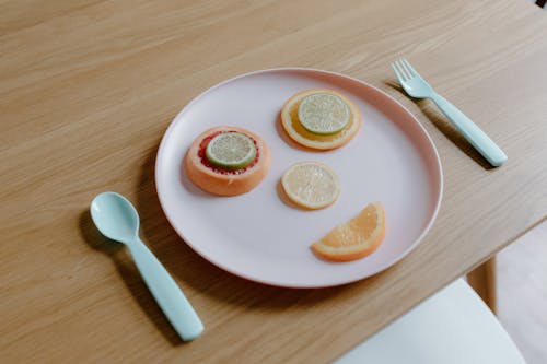 From above of plastic plate with sliced grapefruit orange lemon and lime making face near spoon and fork