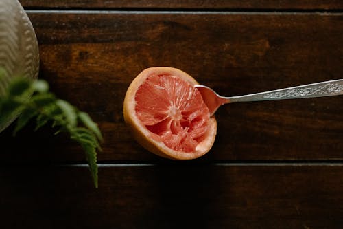 High angle of sour grapefruit with spoon in bright pulp placed on wooden table near plant in vase