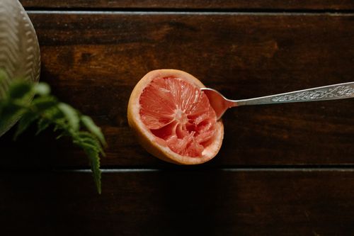Free High angle of sour grapefruit with spoon in bright pulp placed on wooden table near plant in vase Stock Photo