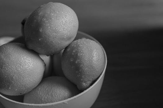 Black and white photo of fresh lemons with water droplets in a bowl. High-angle view for food photography.