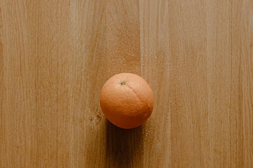Top view of tasty round orange placed on wooden surface in light room