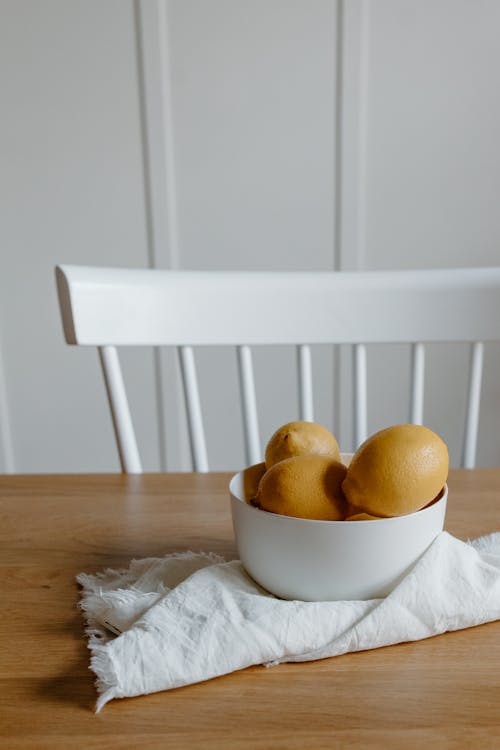 Bowl filled with lemons on textile on table near chair